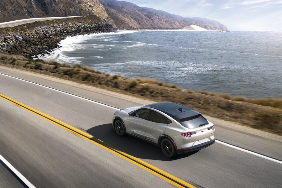 A silver Ford Mustang Mach E drives along a coastal highway